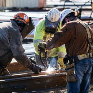 Three construction workers cooperating to weld metal girders together